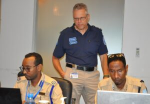 Suomalaisen poliisin virkapukuun pukeutunut henkilö katsoo taustalla kahden somalialaisen kollegansa työskentelyä tietokoneilla.